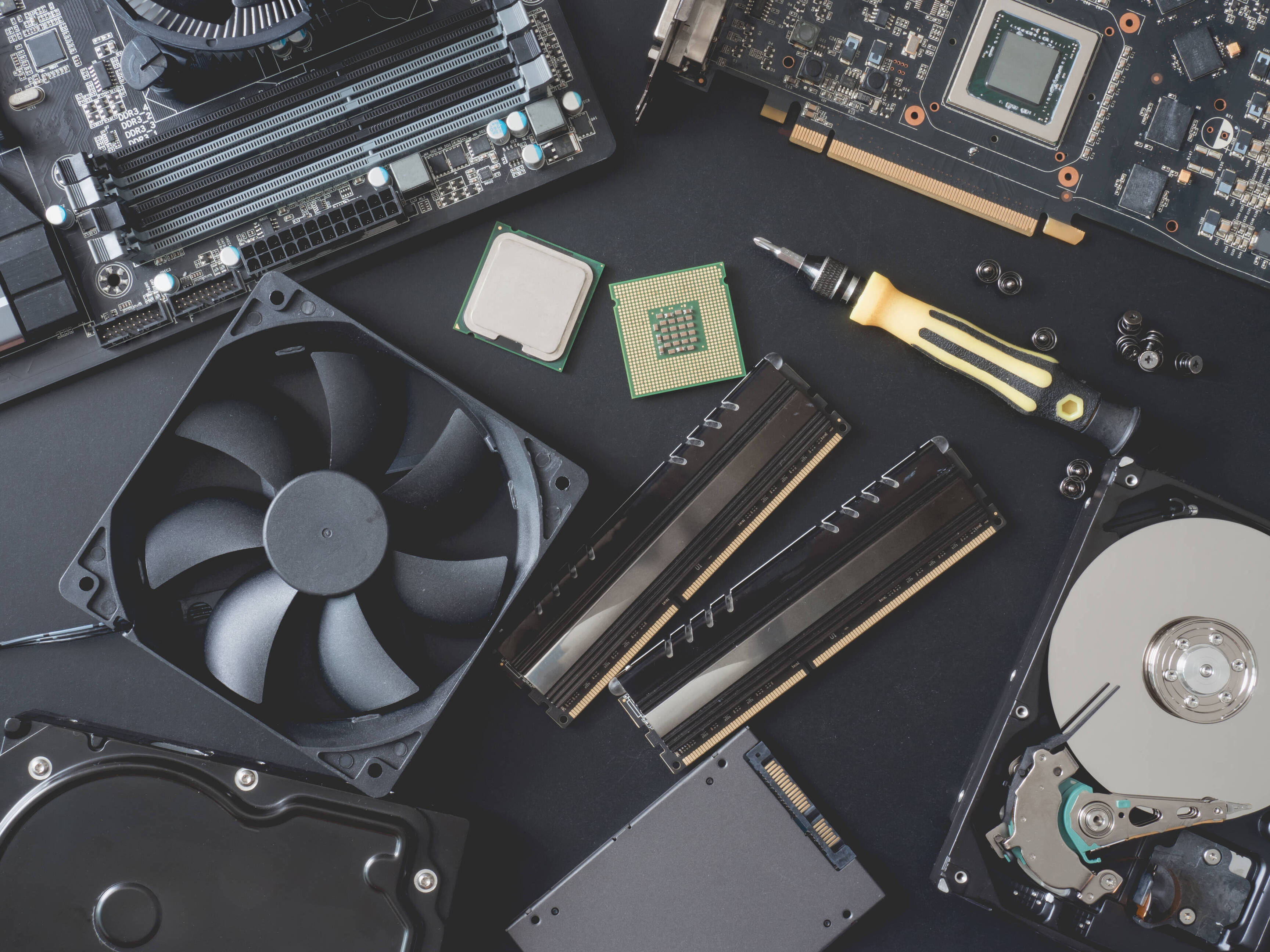 top view of computer parts with harddisk, ram, CPU, graphics card, SSD(solid state drive), motherboard, tools and Fan case on black steel background.