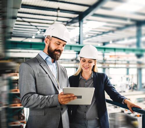 A portrait of a mature industrial man and woman engineer with tablet in a factory, working.